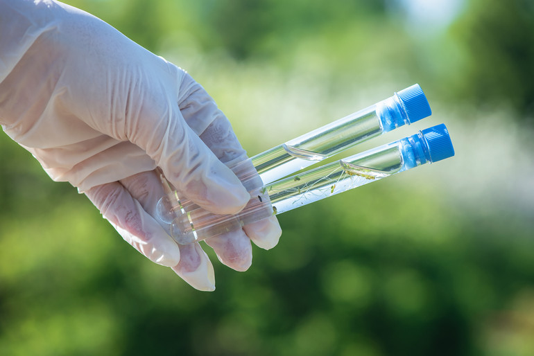 Scientist is holding in hands a clear and dirty water test tubes close up.